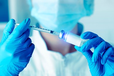 Laboratory worker filling syringe with medication from glass vial in hospital, closeup. Color toned