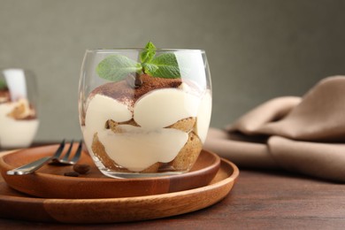 Delicious tiramisu in glass, mint leaves, coffee beans and fork on wooden table, closeup. Space for text