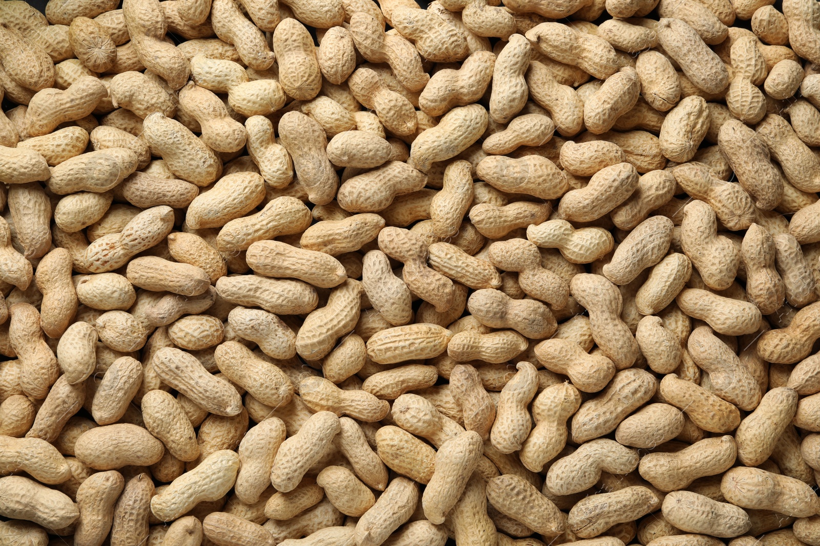 Photo of Many fresh unpeeled peanuts as background, top view