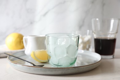 Photo of Making iced coffee. Ice cubes in glass and spoon on white wooden table, closeup