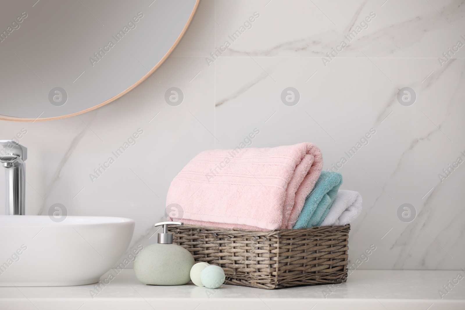 Photo of Basket with fresh towels, soap dispenser and bath bombs on countertop indoors