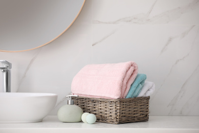 Basket with fresh towels, soap dispenser and bath bombs on countertop indoors