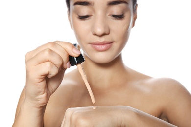 Photo of Young woman testing liquid foundation on her hand against white background