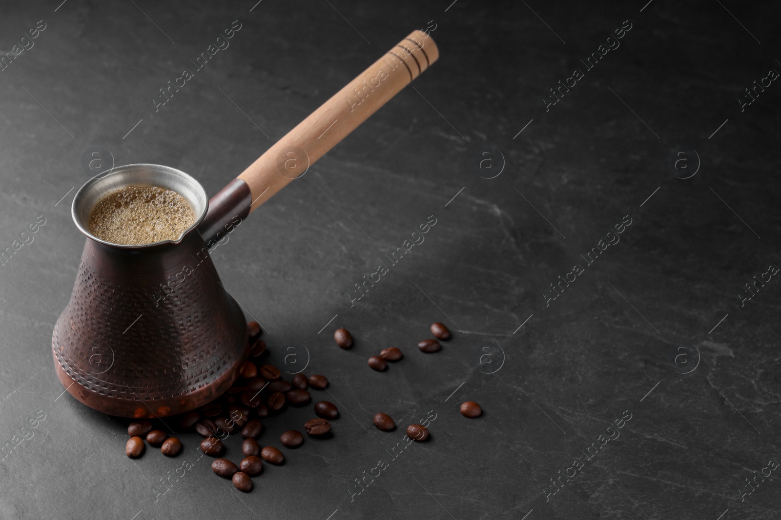 Photo of Cezve with Turkish coffee and beans on dark grey table, space for text