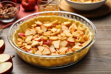 Raw dough with apple slices on wooden table, closeup. Baking pie