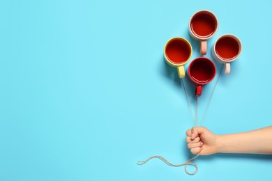 Woman holding threads with cups like balloons on light blue background, top view. Space for text