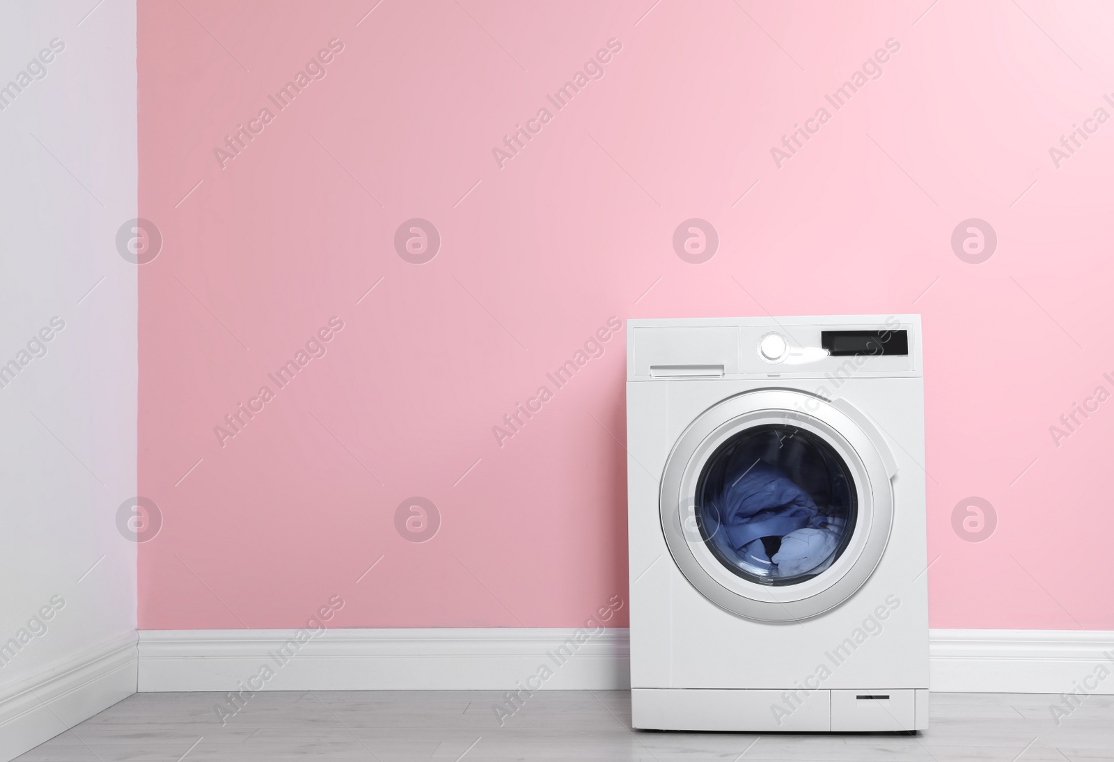 Photo of Washing machine with laundry near color wall. Space for text