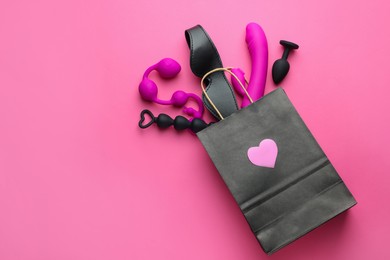 Photo of Shopping bag with different sex toys on pink background, flat lay. Space for text