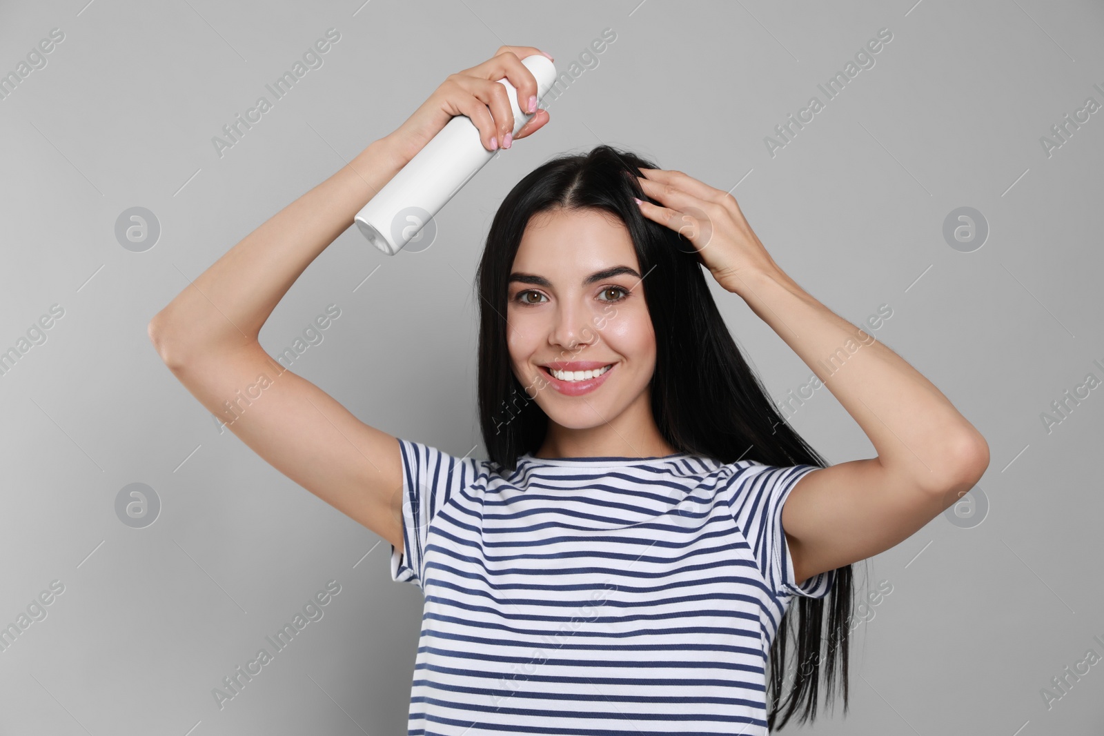 Photo of Woman applying dry shampoo onto her hair on light grey background