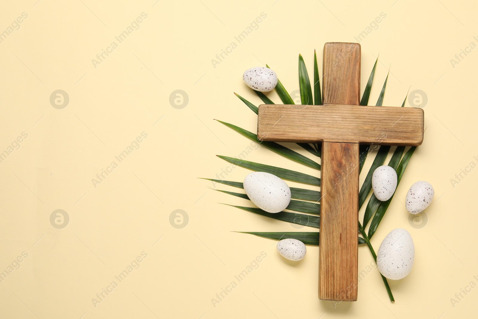 Photo of Wooden cross, painted Easter eggs and palm leaf on beige background, flat lay. Space for text