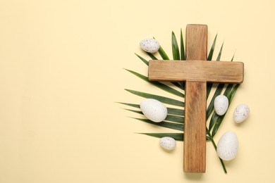 Wooden cross, painted Easter eggs and palm leaf on beige background, flat lay. Space for text