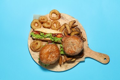 Photo of Tasty burgers, hot dog, potato wedges and fried onion rings on light blue background, top view. Fast food