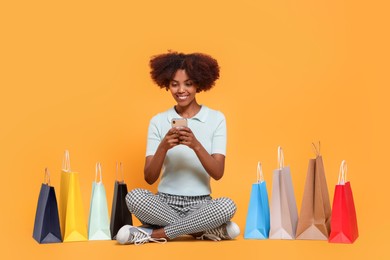 Photo of Happy African American woman with shopping bags and smartphone on orange background