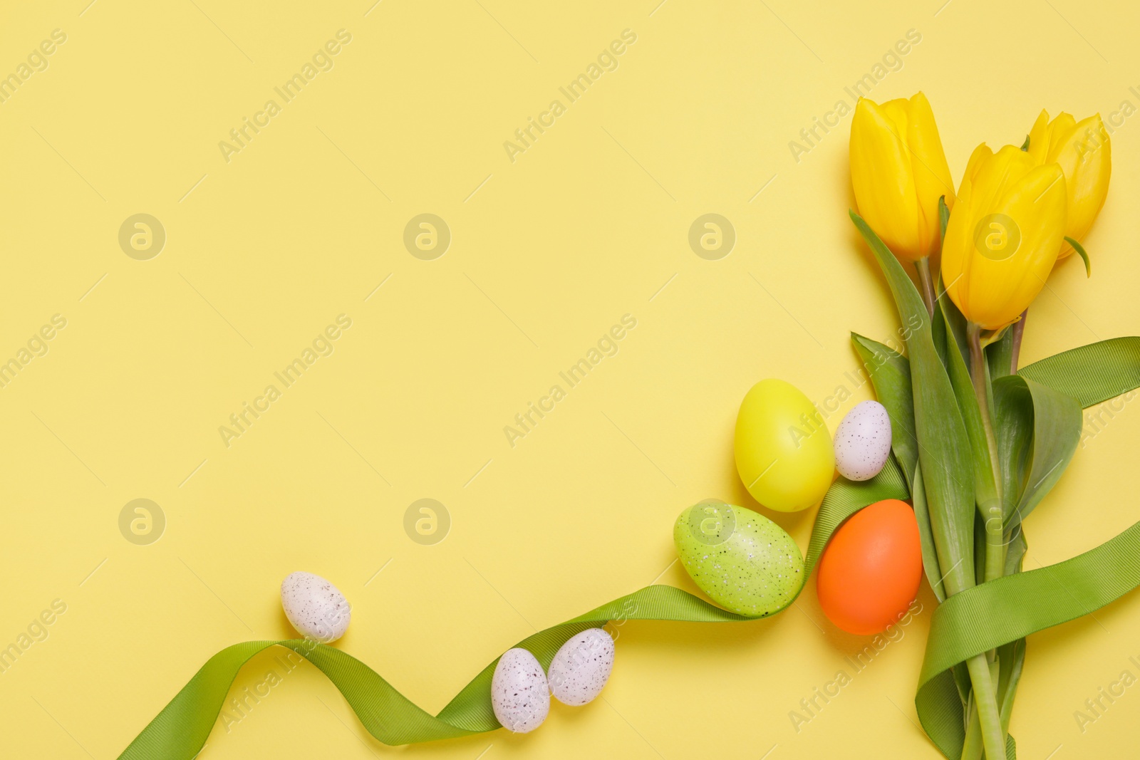 Photo of Flat lay composition of painted Easter eggs and tulip flowers on yellow background. Space for text