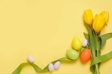 Photo of Flat lay composition of painted Easter eggs and tulip flowers on yellow background. Space for text