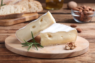 Photo of Tasty cut brie cheese with rosemary and walnut on wooden table