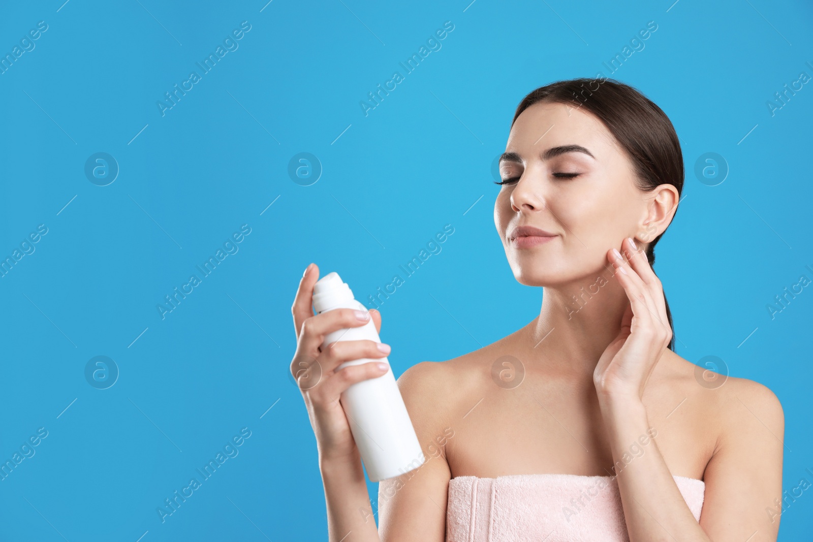 Photo of Young woman applying thermal water on face against color background, space for text. Cosmetic product