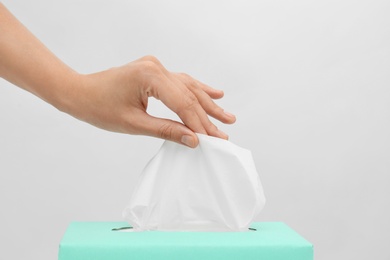 Woman taking paper tissue from box on light background, closeup