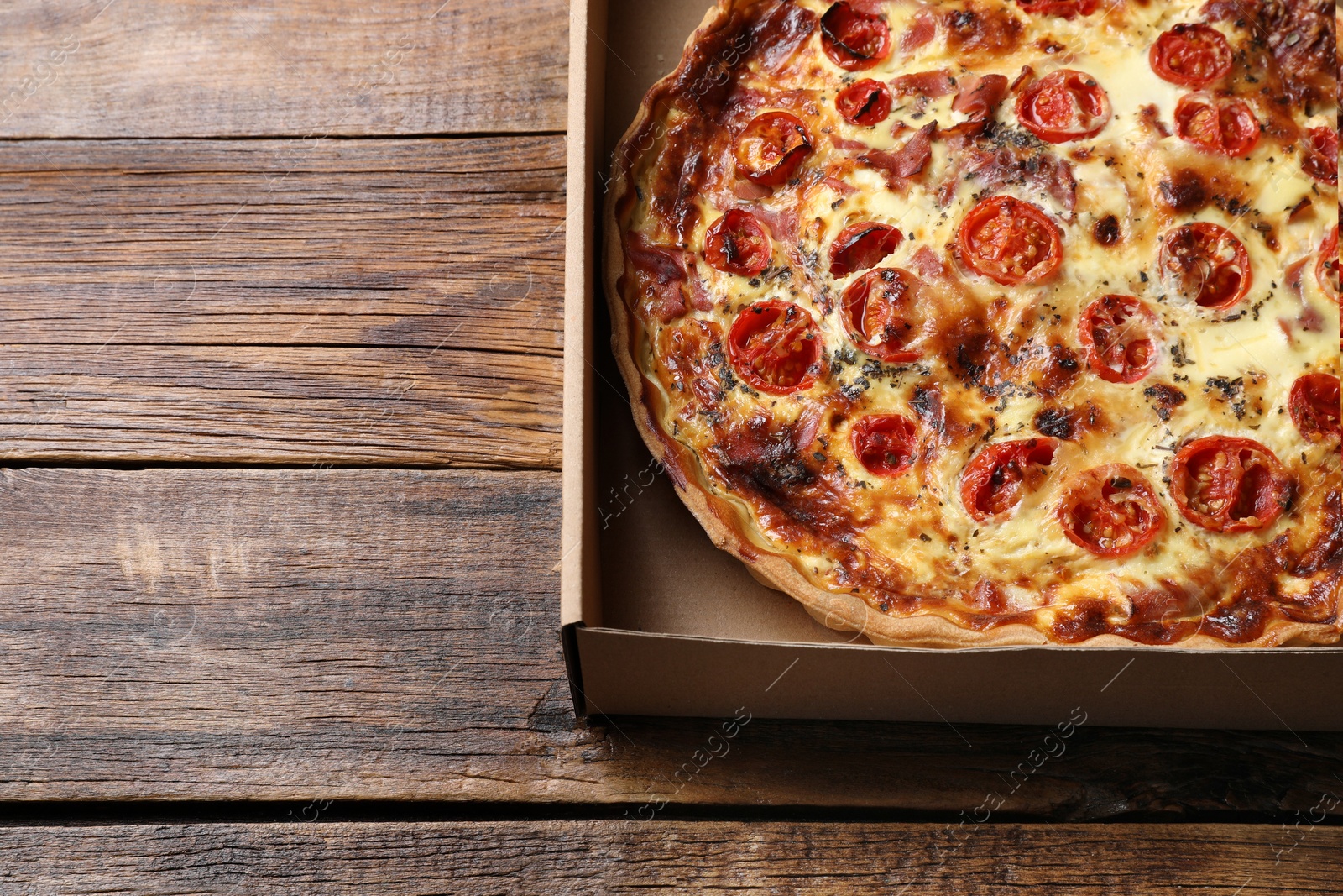 Photo of Delicious quiche with prosciutto and tomatoes in delivery box on wooden table, top view. Space for text