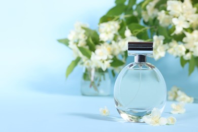 Photo of Aromatic perfume in bottle and beautiful jasmine flowers on light blue background, closeup. Space for text