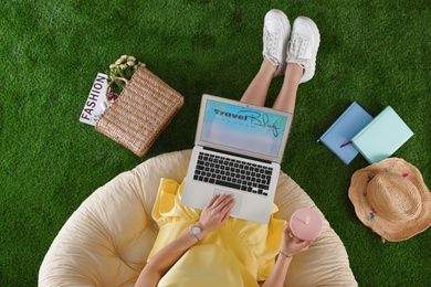 Woman and laptop with travel blogger site on artificial grass, top view