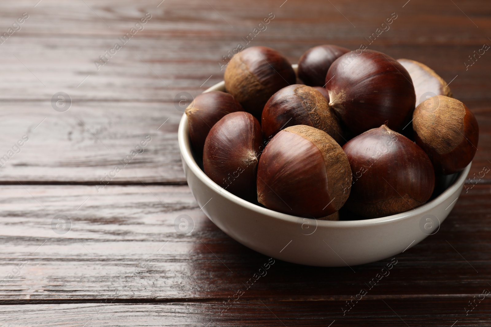 Photo of Sweet fresh edible chestnuts in bowl on wooden table, closeup. Space for text