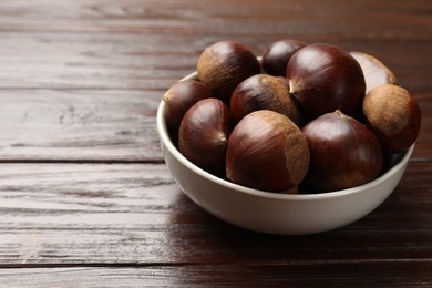 Sweet fresh edible chestnuts in bowl on wooden table, closeup. Space for text