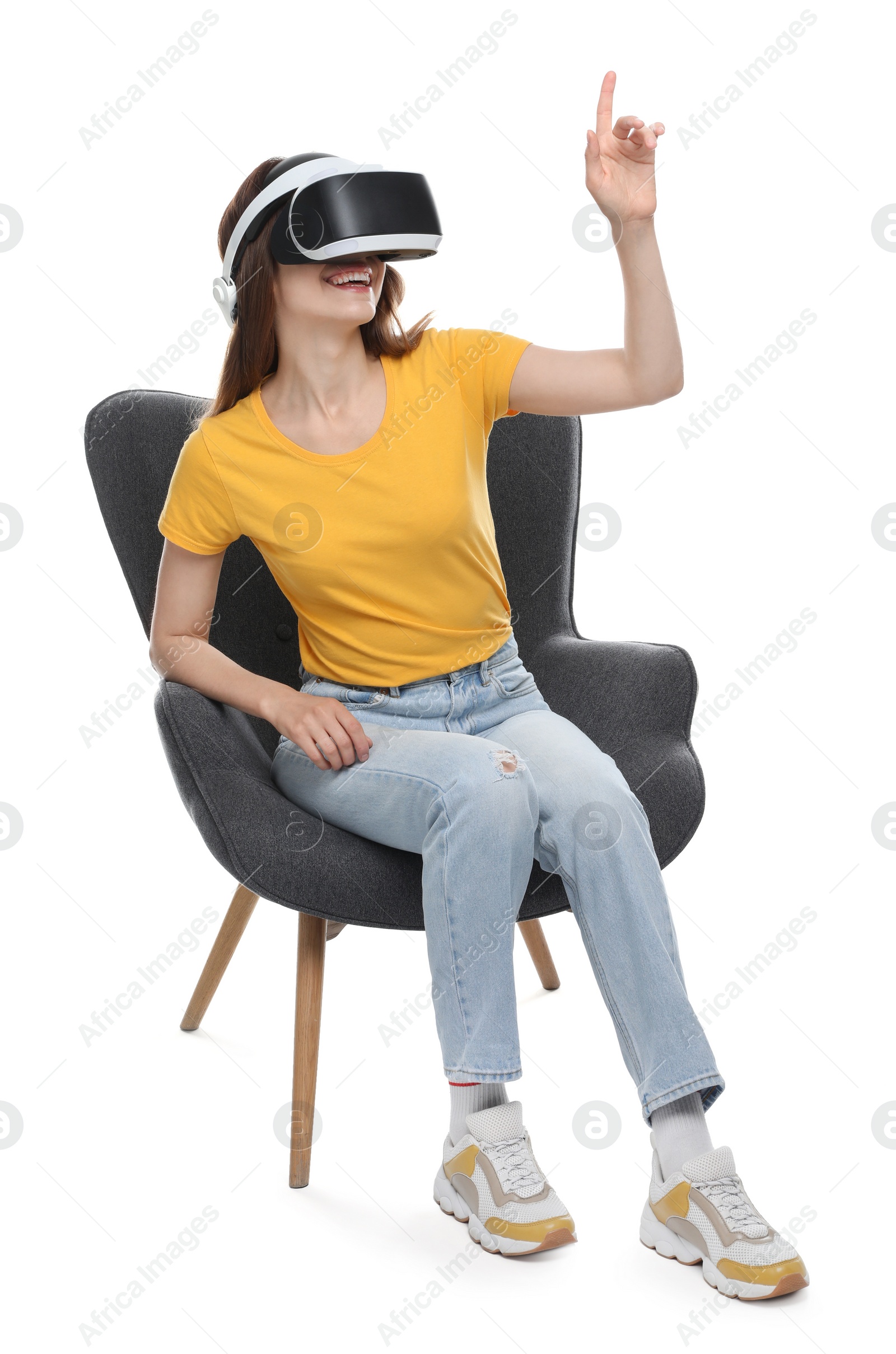 Photo of Smiling woman using virtual reality headset while sitting in armchair against white background