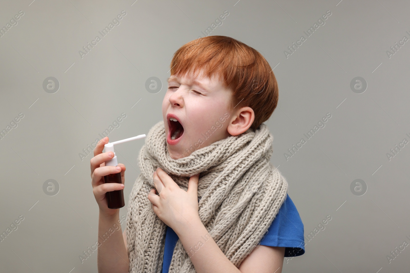 Photo of Little boy with scarf using throat spray on grey background