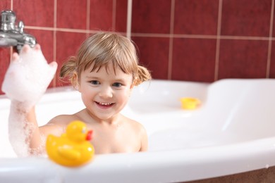 Photo of Smiling girl bathing with toy duck in tub at home, space for text