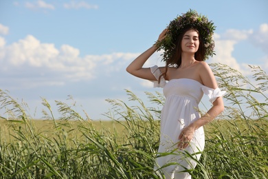 Young woman wearing wreath made of beautiful flowers in field on sunny day