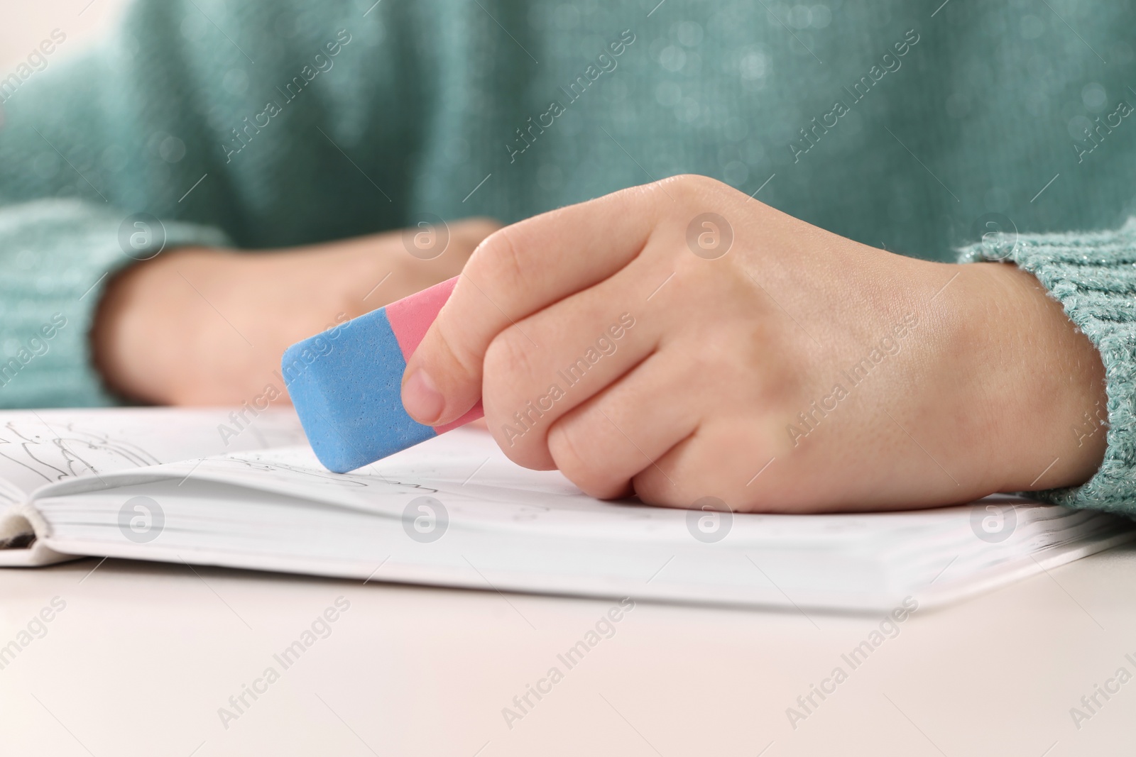 Photo of Girl using eraser at white desk, closeup