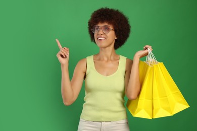Happy young woman with shopping bags pointing at something on green background