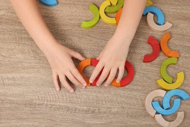 Photo of Motor skills development. Girl playing with colorful arcs at wooden table, top view