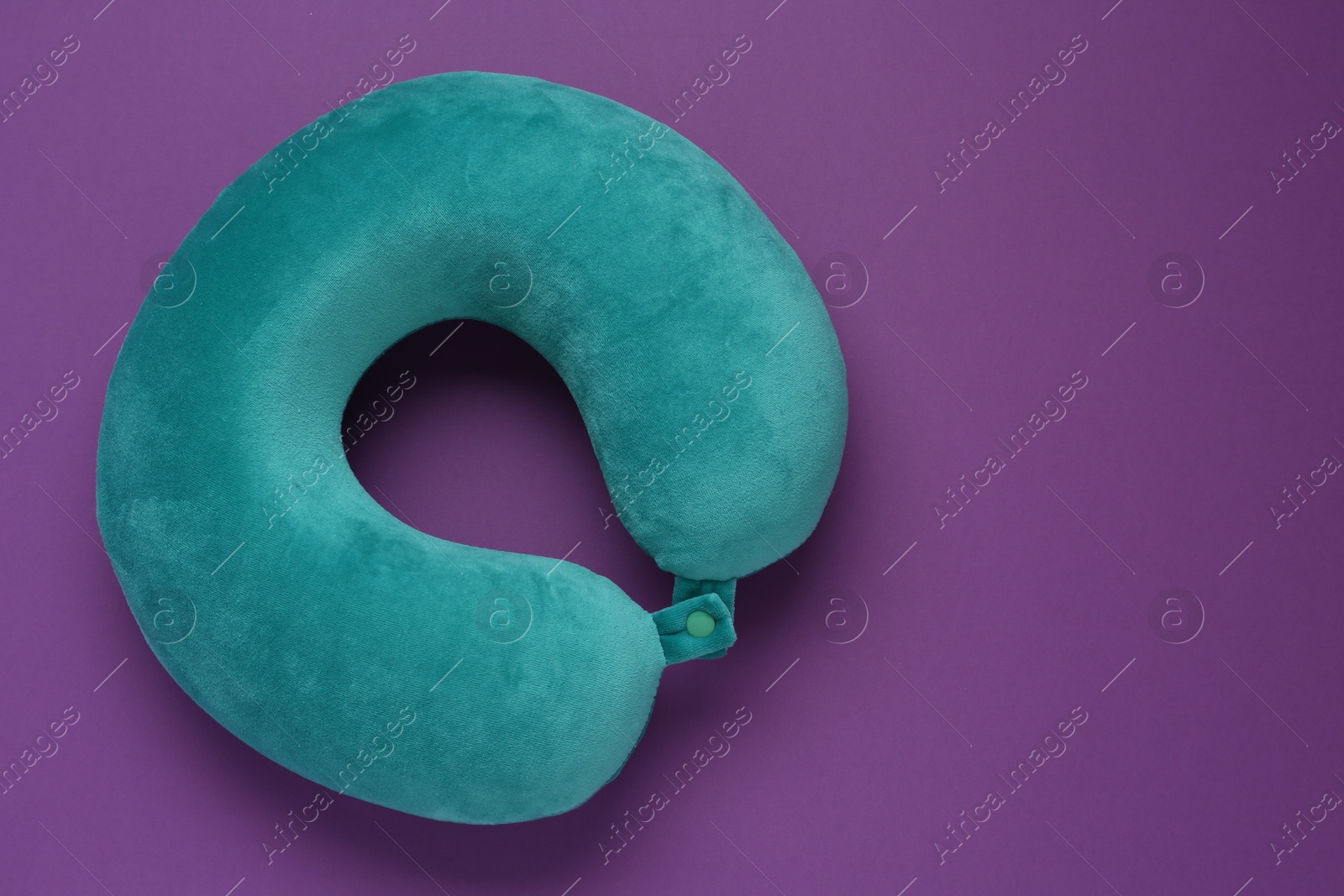 Photo of Turquoise travel pillow on purple background, top view. Space for text