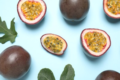 Photo of Fresh ripe passion fruits (maracuyas) with green leaves on light blue background, flat lay