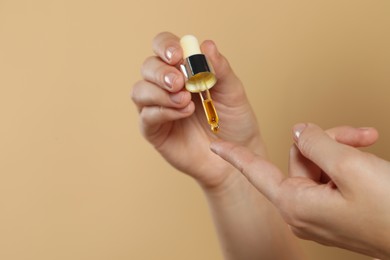Photo of Young woman applying essential oil onto finger on beige background, closeup. Space for text