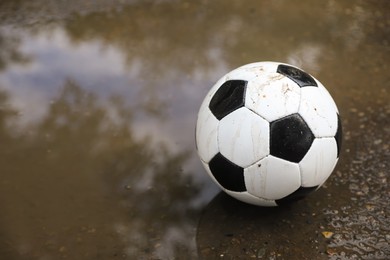 Photo of Soccer ball near puddle outdoors, space for text