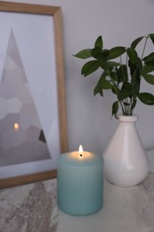 Beautiful burning candle and vase with green branches on marble table