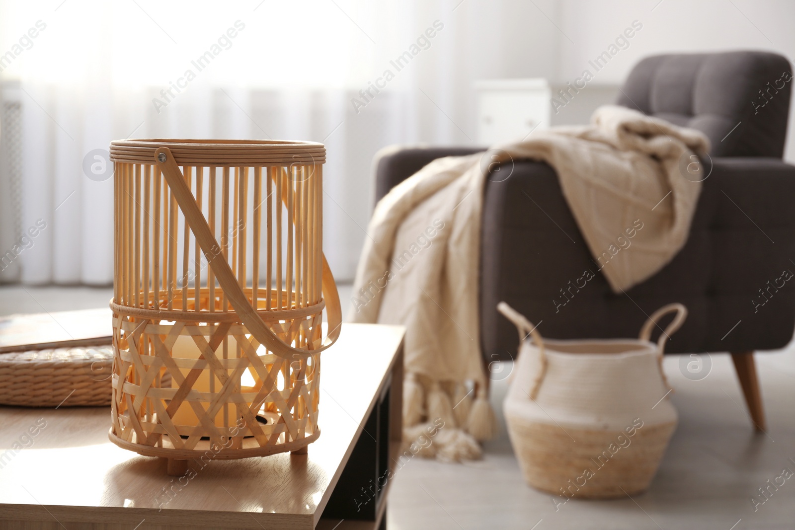 Photo of Stylish wicker holder with candle on wooden table indoors, space for text