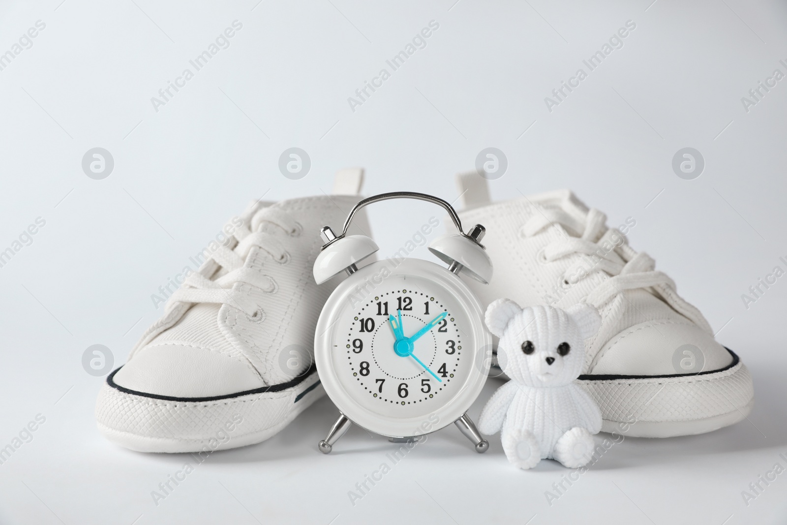 Photo of Alarm clock, toy bear and baby booties on white background. Time to give birth