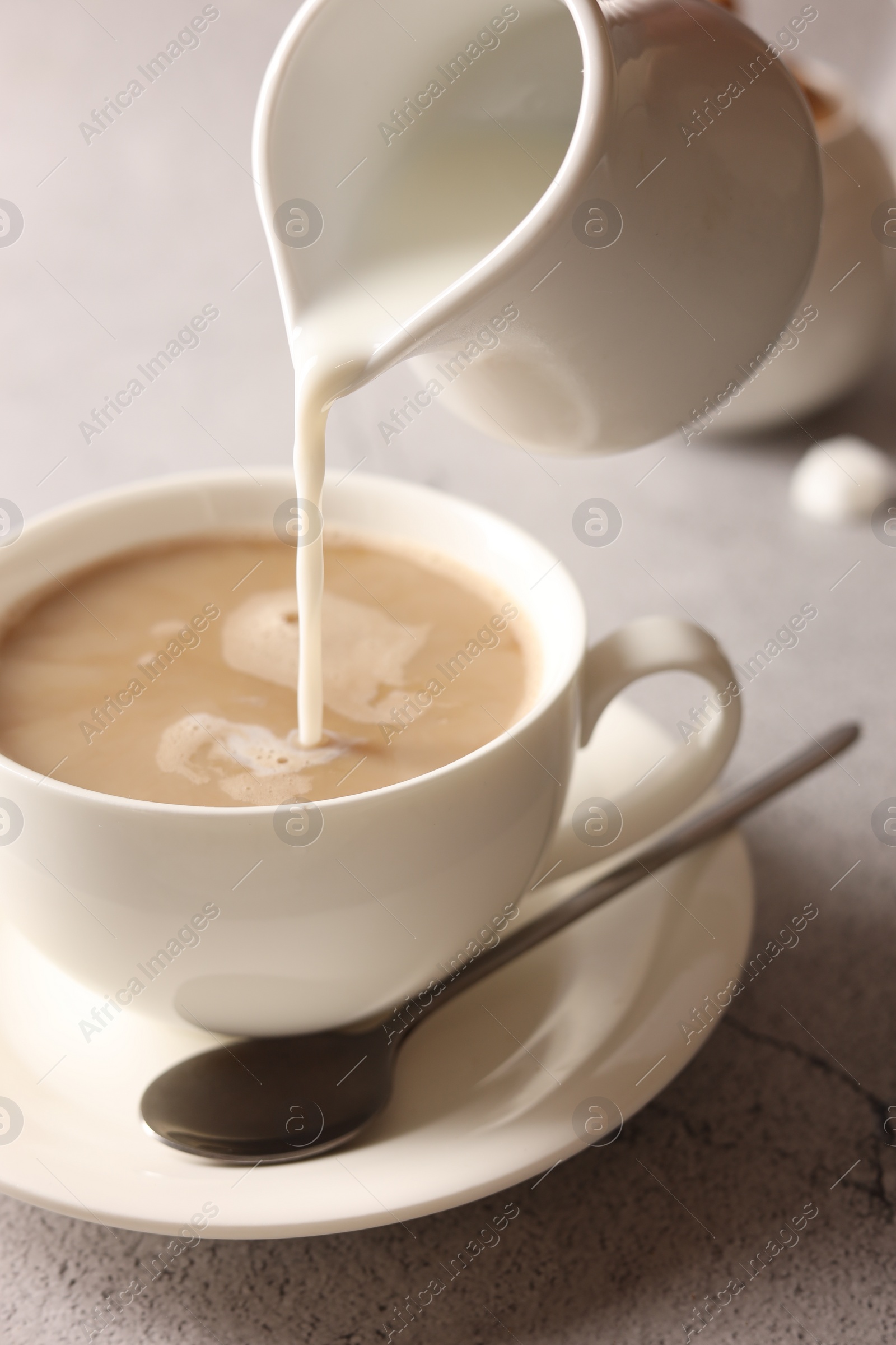 Photo of Pouring milk into cup with coffee on light grey textured table, closeup