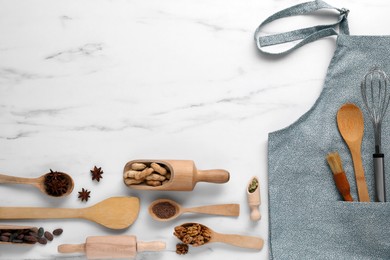 Flat lay composition with grey apron, ingredients and kitchen utensils on white marble table. Space for text