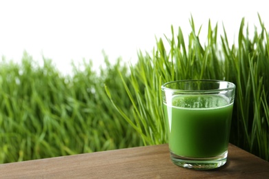 Photo of Glass of juice on table and fresh wheat grass against white background. Space for text