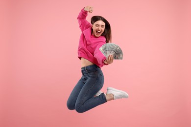 Photo of Happy woman with dollar banknotes jumping on pink background