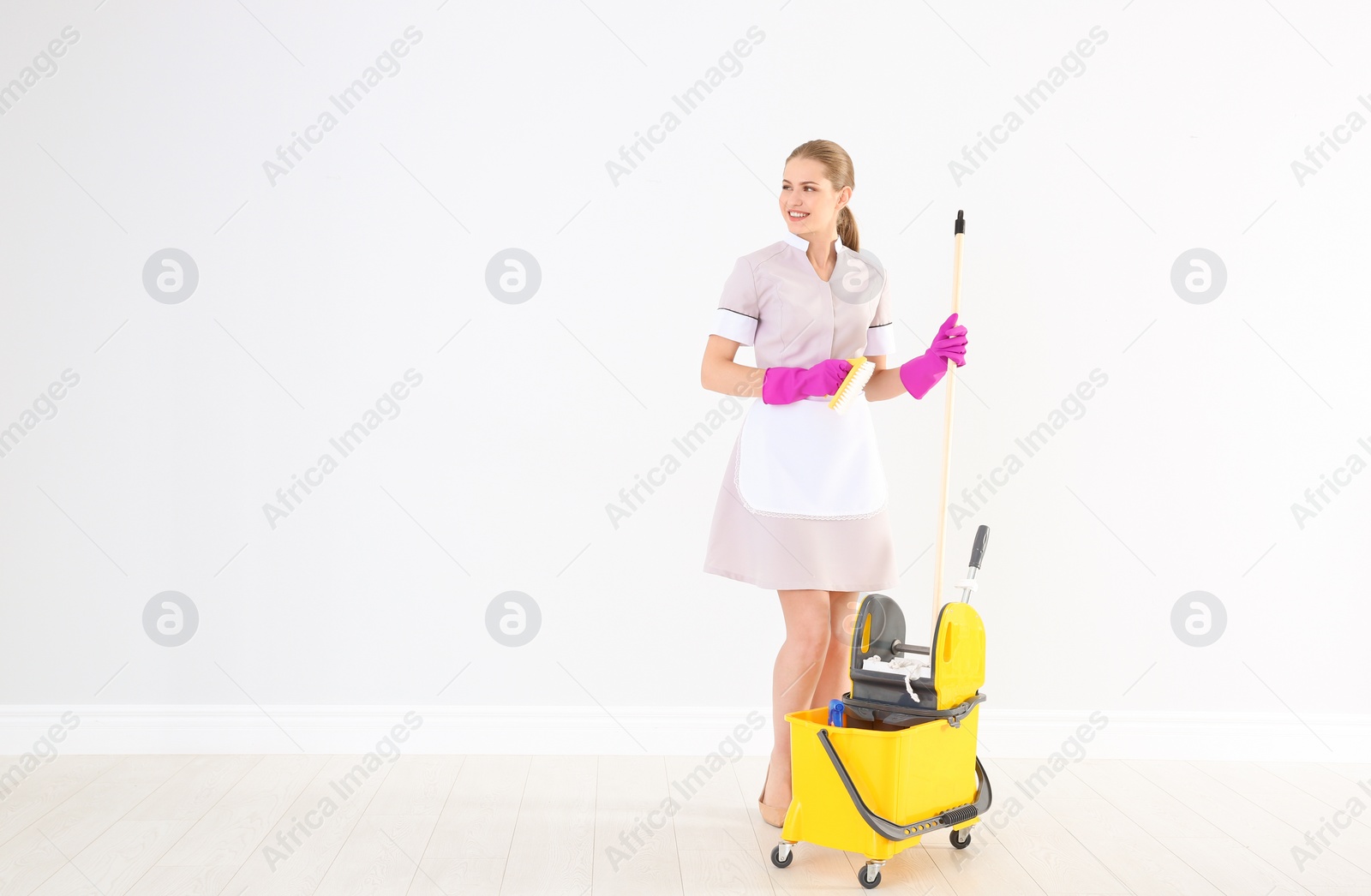 Photo of Young chambermaid with cleaning supplies indoors