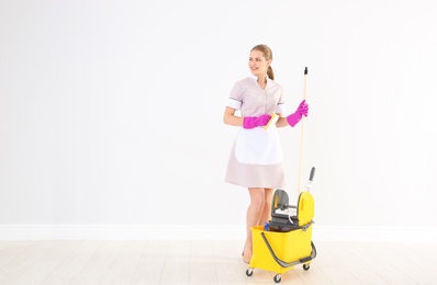 Young chambermaid with cleaning supplies indoors