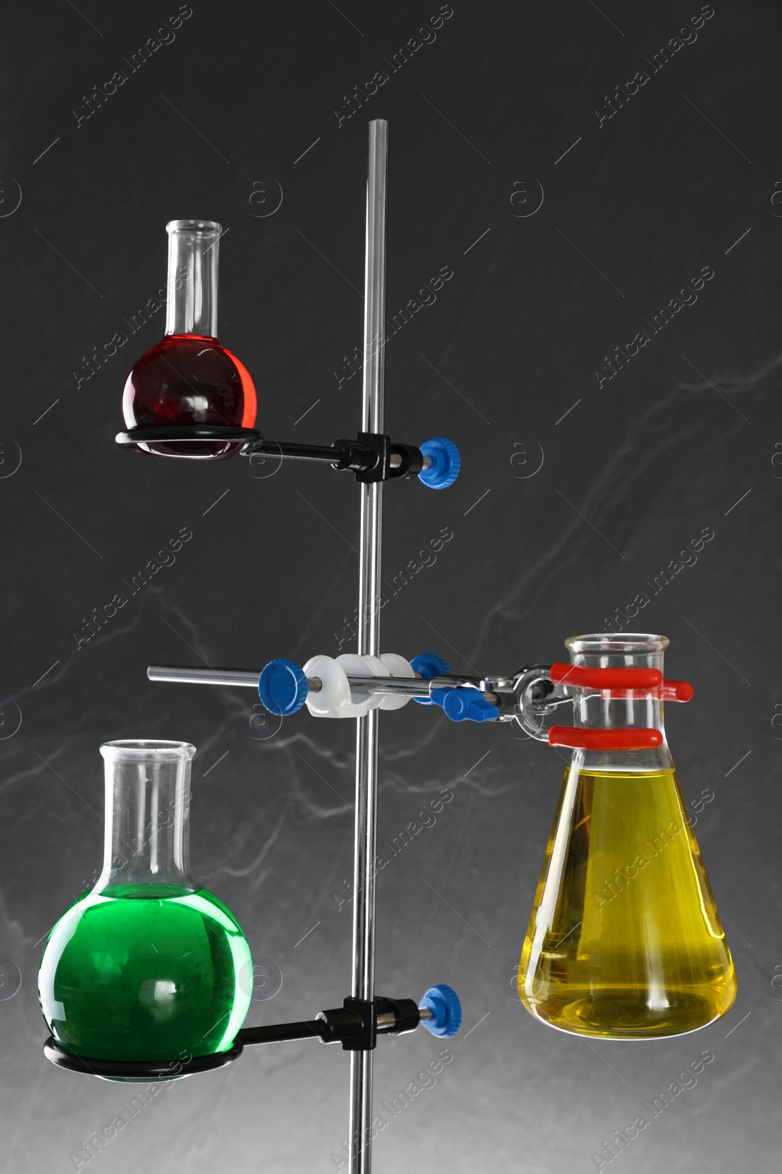 Photo of Retort stand and laboratory flasks with liquids on grey background