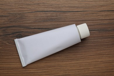 Photo of Blank white tube of ointment on wooden table, top view. Space for text