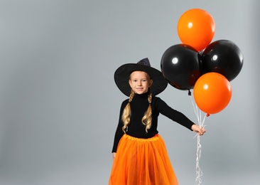 Cute little girl with balloons wearing Halloween costume on grey background